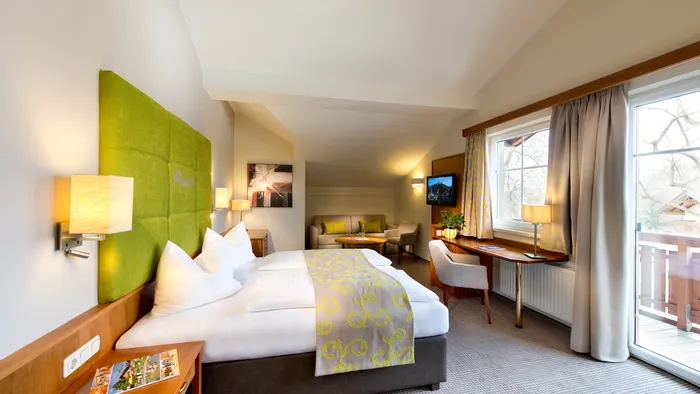 Modern hotel room with green headboard, double bed, desk, sofa area and balcony access